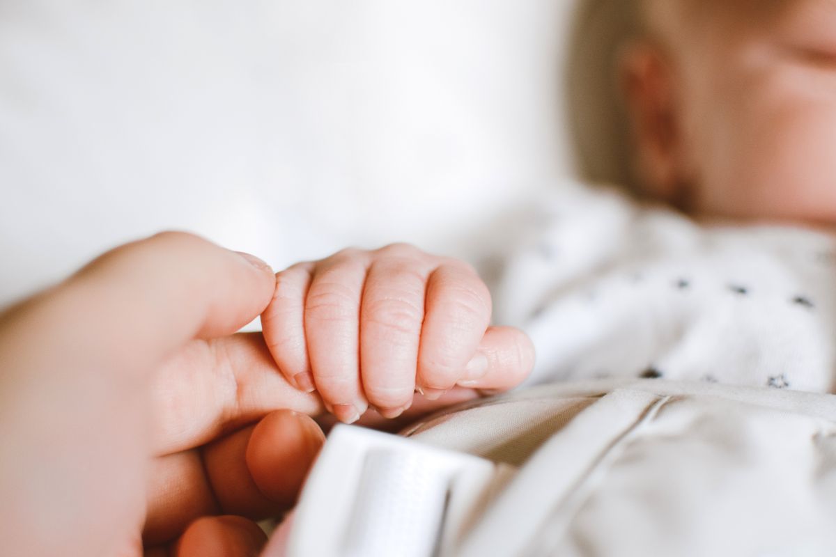 A newborn's hand gripping a parent's finger